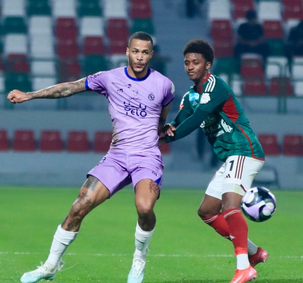 Two soccer players in purple uniforms engaged in a dynamic match on the field, showcasing their athleticism and teamwork.